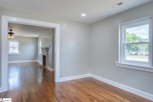 spare room with dark hardwood / wood-style floors, ceiling fan, a wealth of natural light, and a brick fireplace