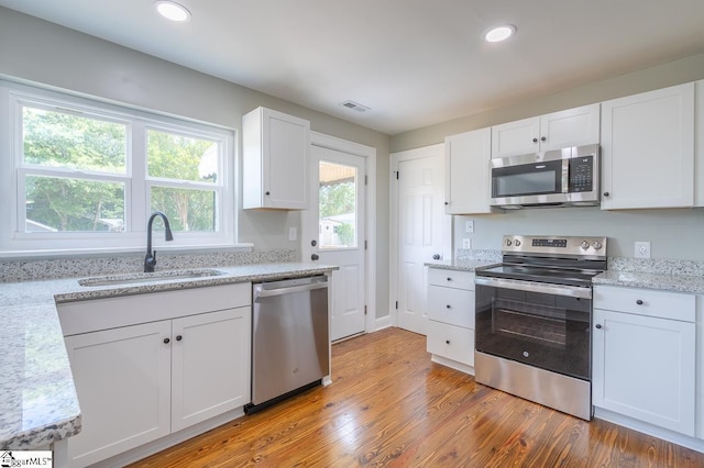 kitchen with light stone countertops, white cabinetry, sink, stainless steel appliances, and light hardwood / wood-style floors