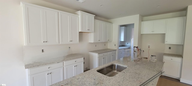 kitchen featuring white cabinetry, an island with sink, and light stone counters