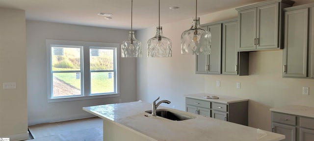 kitchen with light stone countertops, a center island with sink, hanging light fixtures, and sink