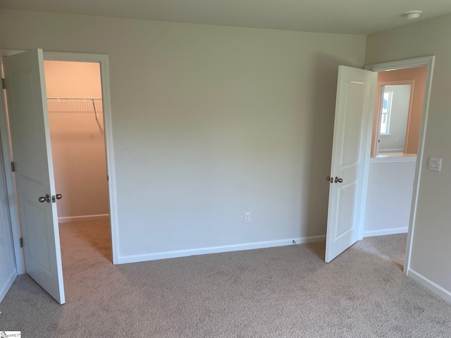 unfurnished bedroom with a walk in closet, a closet, and light colored carpet