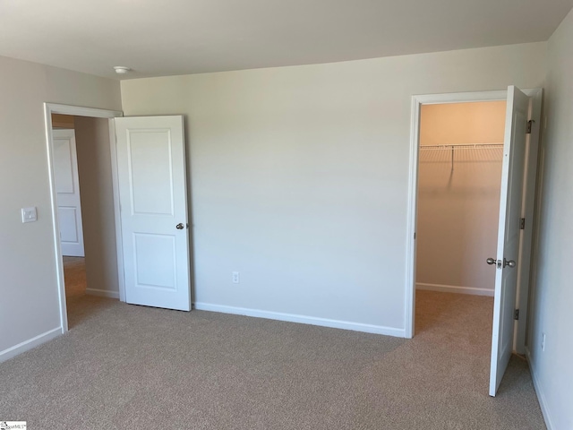 unfurnished bedroom featuring a walk in closet, light carpet, and a closet