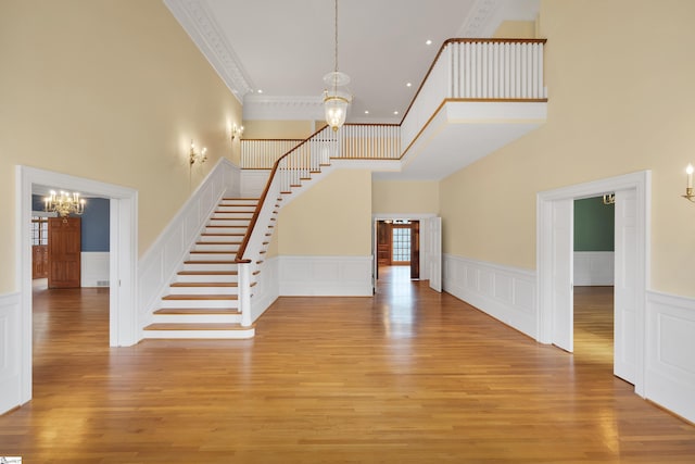 staircase with a high ceiling, a chandelier, crown molding, and hardwood / wood-style floors