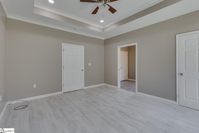 empty room with ceiling fan, ornamental molding, a tray ceiling, and light hardwood / wood-style floors