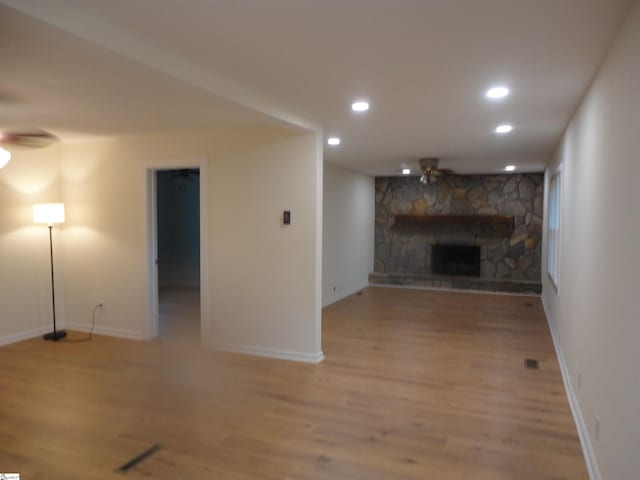 unfurnished living room with a stone fireplace, ceiling fan, and light hardwood / wood-style flooring