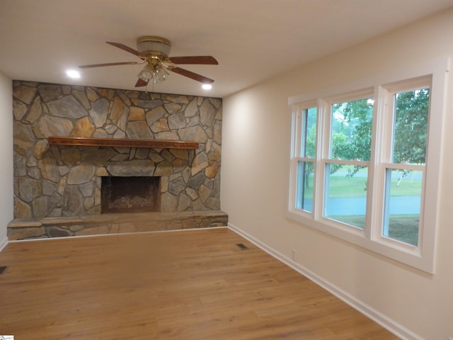 unfurnished living room with a stone fireplace, ceiling fan, and light hardwood / wood-style flooring