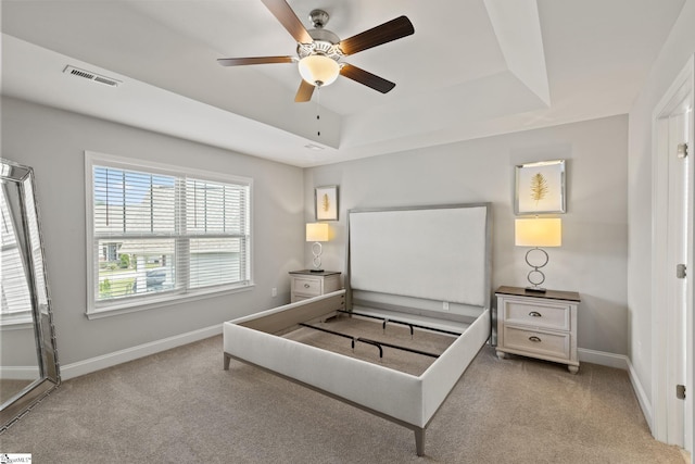 bedroom with a raised ceiling, ceiling fan, and light carpet