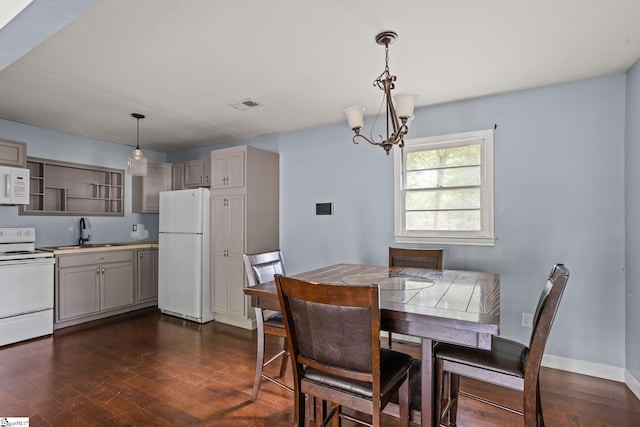 dining space with sink, dark wood-type flooring, and an inviting chandelier