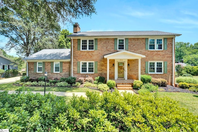 colonial inspired home with brick siding and a chimney