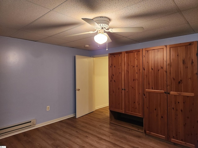 unfurnished bedroom featuring ceiling fan, a baseboard heating unit, a paneled ceiling, and dark hardwood / wood-style flooring