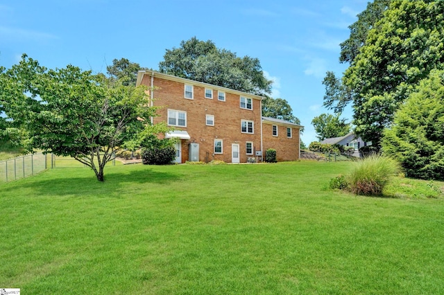 rear view of house with brick siding, a yard, and fence