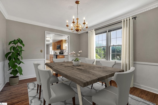 dining area with dark wood-type flooring, a wainscoted wall, crown molding, and an inviting chandelier