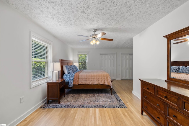 bedroom with two closets, ceiling fan, a textured ceiling, and light wood-type flooring