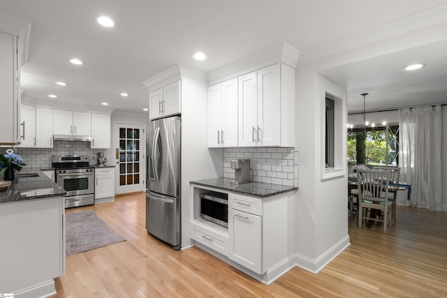 kitchen featuring backsplash, hanging light fixtures, appliances with stainless steel finishes, light hardwood / wood-style floors, and white cabinetry