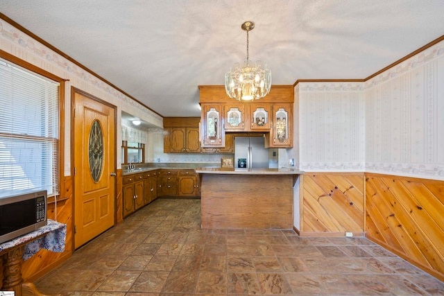 kitchen with pendant lighting, appliances with stainless steel finishes, a textured ceiling, sink, and wood walls