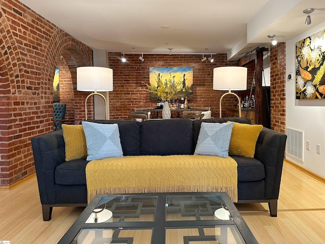 living room with brick wall, hardwood / wood-style floors, and rail lighting