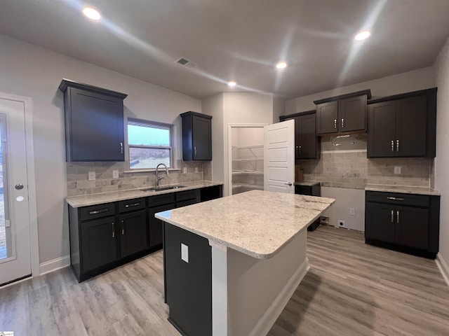 kitchen featuring sink, light hardwood / wood-style floors, tasteful backsplash, a kitchen island, and a breakfast bar area