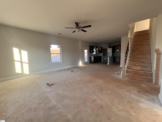 unfurnished living room with concrete floors, ceiling fan, baseboards, and stairs