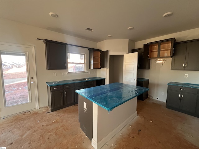 kitchen featuring a center island, open shelves, dark countertops, visible vents, and a sink