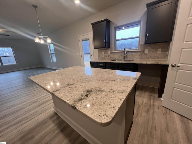 kitchen featuring light stone counters, a center island, backsplash, a sink, and light wood-type flooring