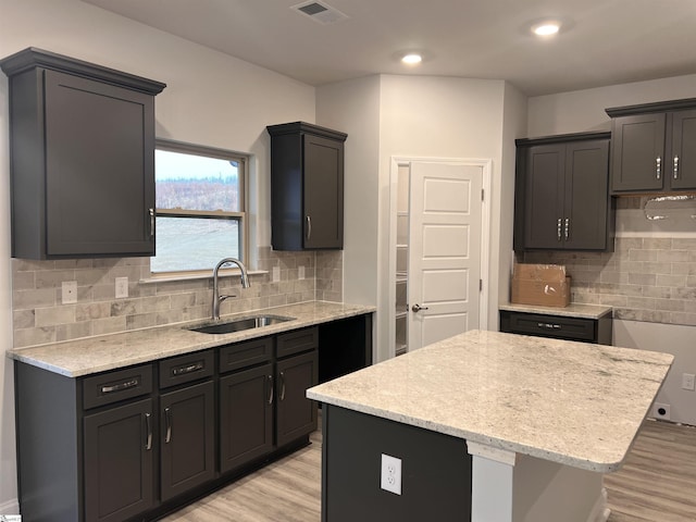 kitchen featuring light wood-type flooring, a center island, visible vents, and a sink