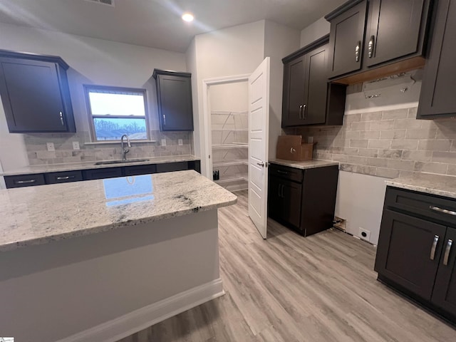 kitchen with light wood-style floors, tasteful backsplash, light stone counters, and a sink