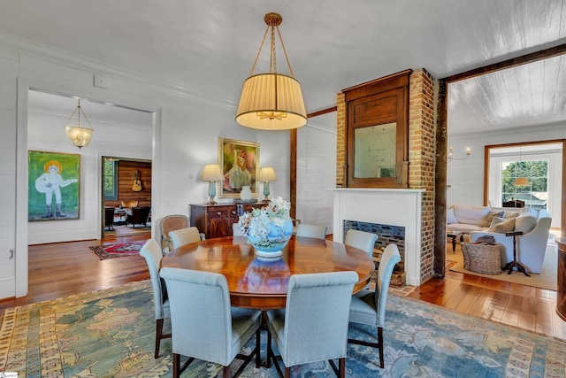 dining room with brick wall, hardwood / wood-style flooring, ornamental molding, and a large fireplace