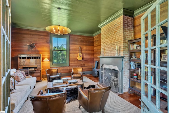 living room featuring wood-type flooring, a chandelier, ornamental molding, wood walls, and a brick fireplace