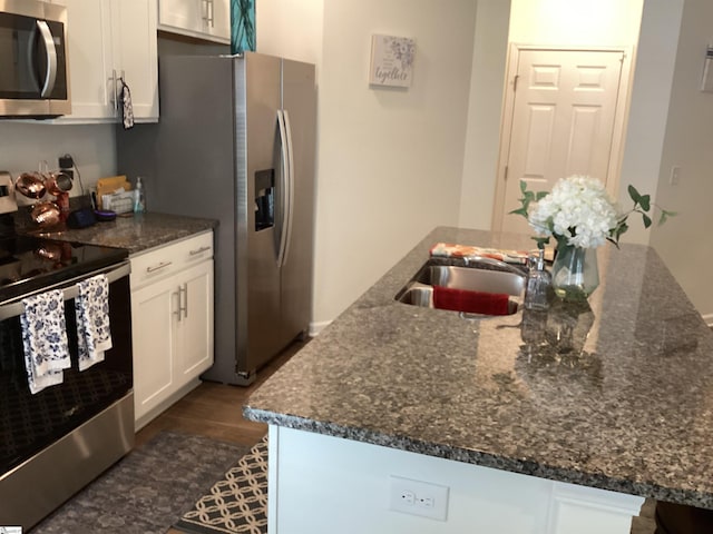 kitchen with white cabinets, dark hardwood / wood-style flooring, appliances with stainless steel finishes, and a center island with sink