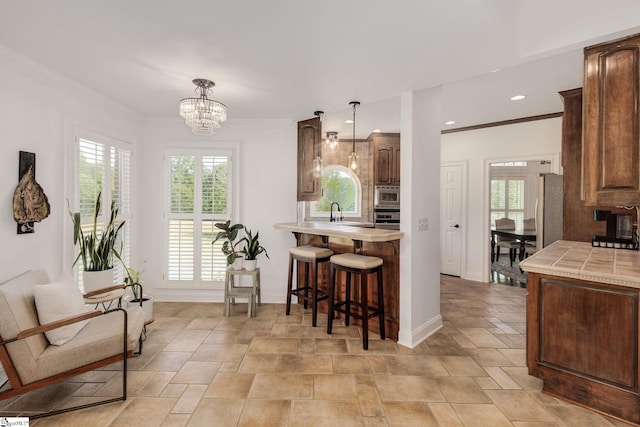 kitchen with crown molding, a chandelier, tile counters, pendant lighting, and stainless steel appliances