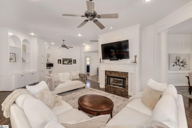 living room with a premium fireplace, ceiling fan, ornamental molding, ornate columns, and dark wood-type flooring