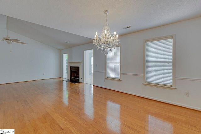 unfurnished living room with lofted ceiling, ceiling fan with notable chandelier, light wood-type flooring, and a healthy amount of sunlight