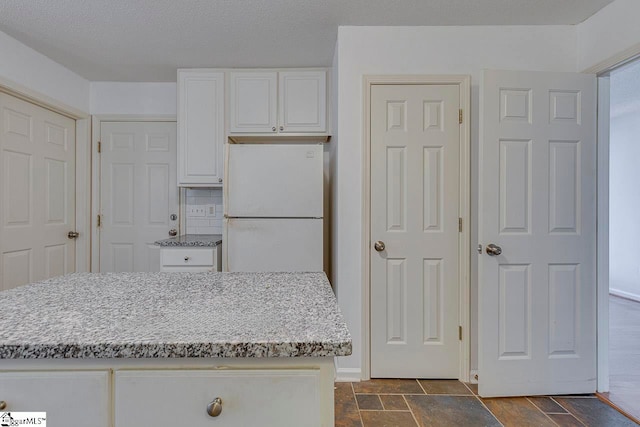 kitchen featuring white cabinets, tile patterned flooring, backsplash, light stone countertops, and white fridge