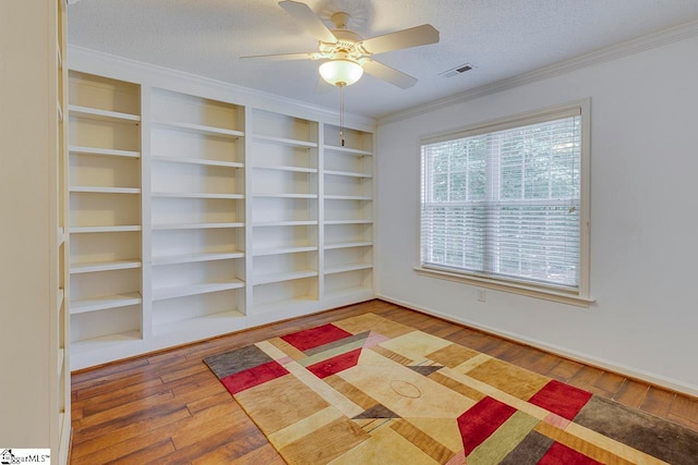 empty room featuring crown molding, light hardwood / wood-style flooring, a textured ceiling, built in shelves, and ceiling fan