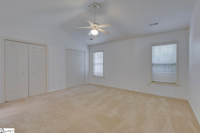 unfurnished bedroom featuring multiple windows, lofted ceiling, and light colored carpet