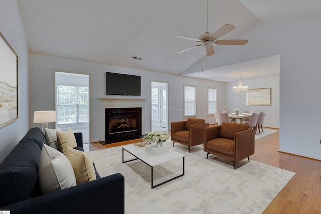 living room featuring light hardwood / wood-style floors, ceiling fan with notable chandelier, and vaulted ceiling