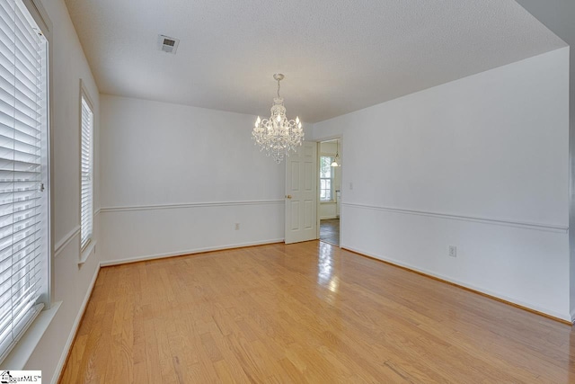 unfurnished room featuring an inviting chandelier, a textured ceiling, and light hardwood / wood-style floors