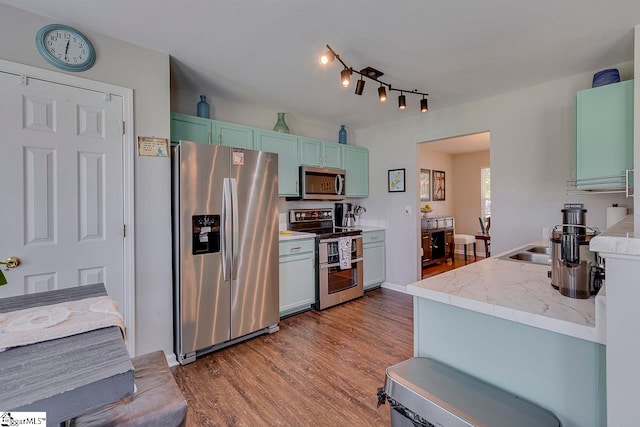 kitchen with appliances with stainless steel finishes, hardwood / wood-style flooring, and track lighting