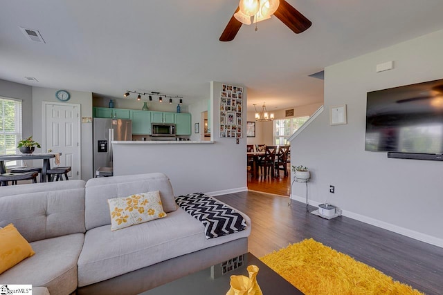 living room featuring ceiling fan with notable chandelier, rail lighting, and dark hardwood / wood-style floors