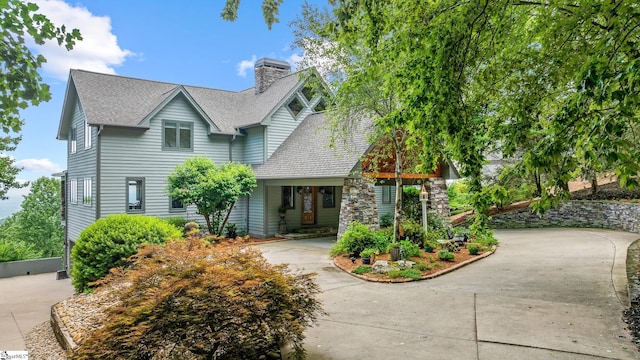 view of front of property featuring concrete driveway, a shingled roof, and a chimney