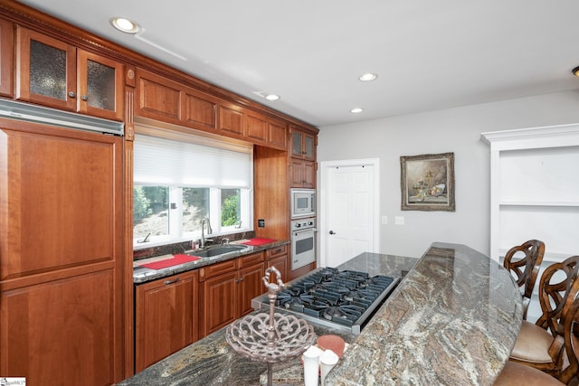 kitchen featuring recessed lighting, appliances with stainless steel finishes, glass insert cabinets, a sink, and dark stone countertops