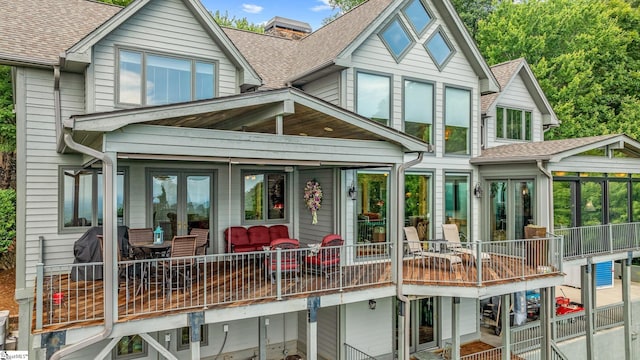 rear view of property featuring a sunroom, roof with shingles, and french doors