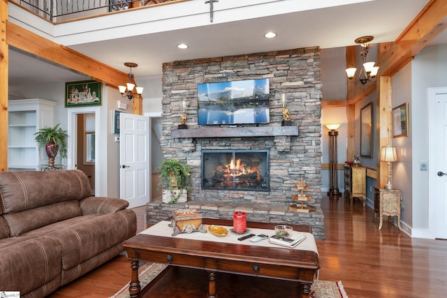 living room featuring beam ceiling, wood-type flooring, a stone fireplace, and a chandelier