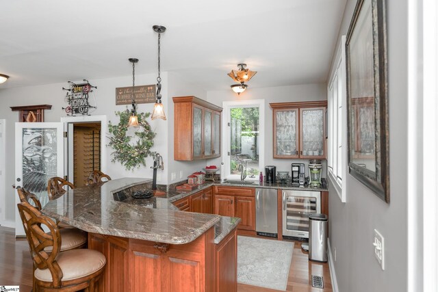 kitchen with light wood-type flooring, sink, beverage cooler, and hanging light fixtures