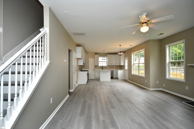 unfurnished living room with sink, ceiling fan with notable chandelier, and light hardwood / wood-style flooring