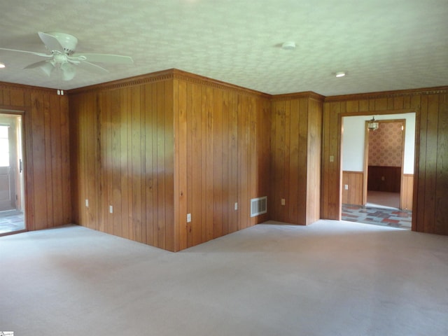 empty room featuring ornamental molding, carpet, ceiling fan, and wood walls