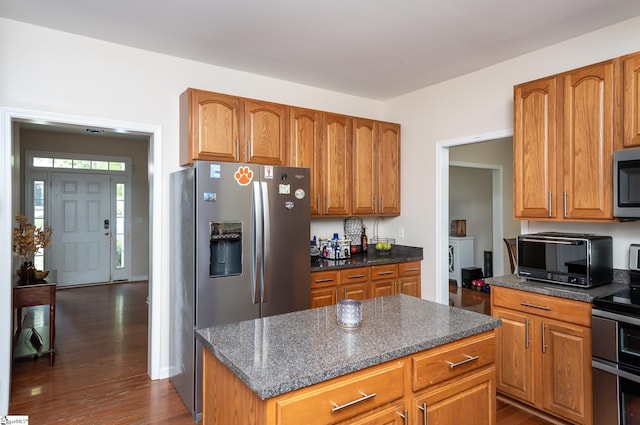 kitchen featuring a kitchen island, appliances with stainless steel finishes, dark wood-type flooring, and dark stone counters