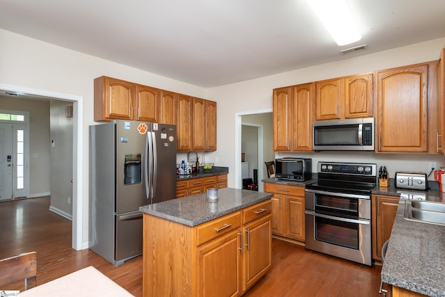 kitchen with stainless steel appliances, a kitchen island, and dark wood-type flooring