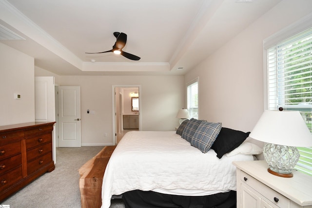 carpeted bedroom with ensuite bathroom, ceiling fan, and a tray ceiling