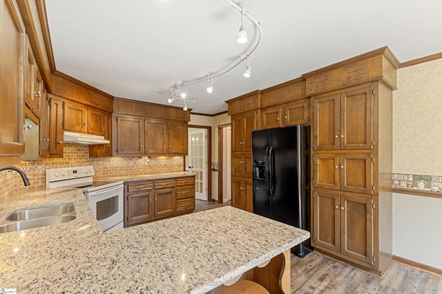 kitchen with sink, light stone counters, black refrigerator with ice dispenser, kitchen peninsula, and white range with electric cooktop